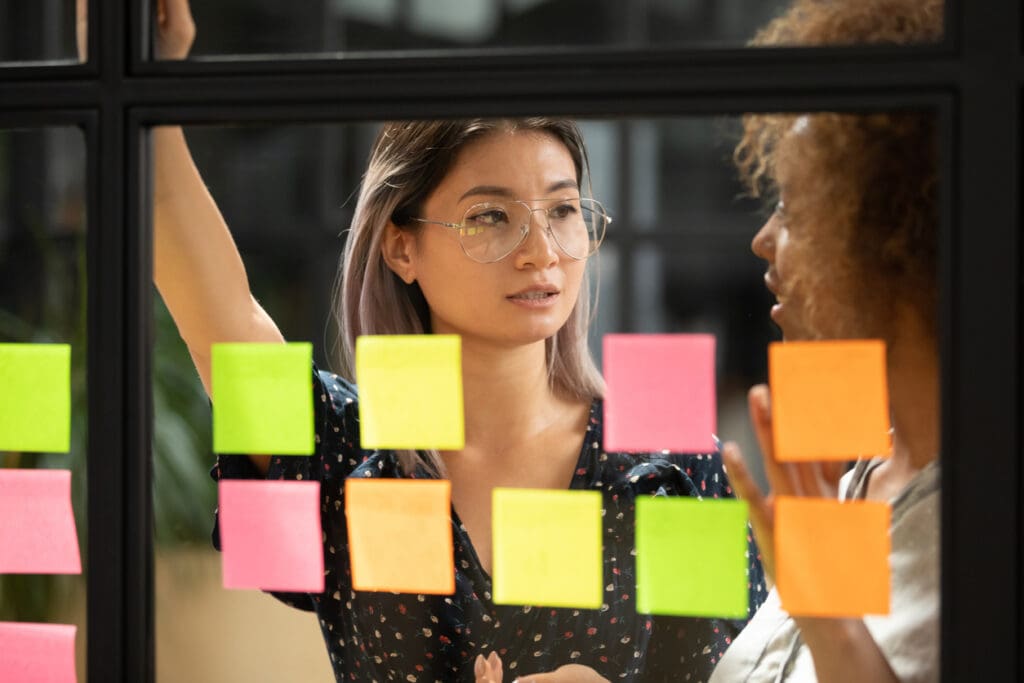Asian businesswoman listen african colleague behind glass with sticky notes